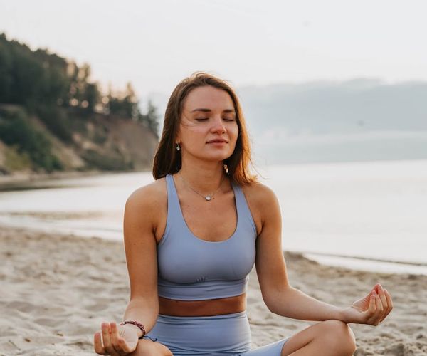 Person meditating peacefully on a yoga mat by the sea at sunrise.
